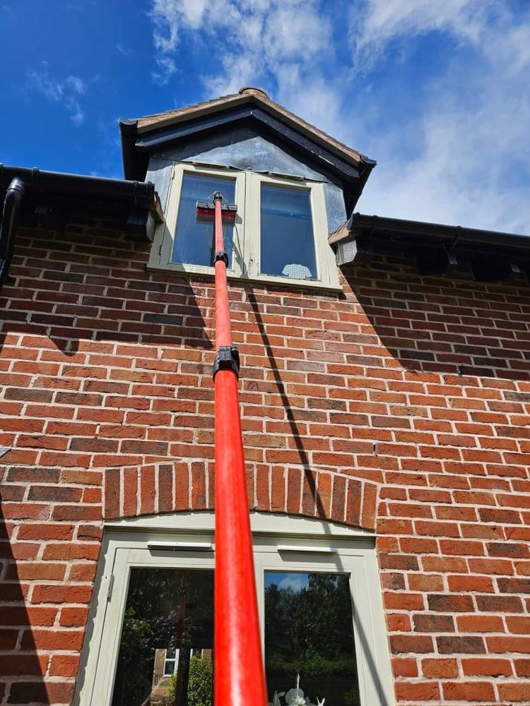 A water fed pole rinsing an upstairs window with pure water, the glass left wet and running clear